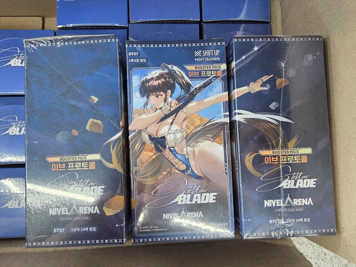 Three 'Nivel Arena - Stella Blade' trading card packs on a cardboard surface with blue boxes in the background.
